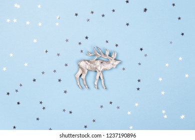 Christmas Figurine Of Reindeer And Silver Confetti On Blue Background. Minimal New Year Card, Top View.