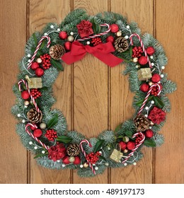 Christmas Fir Wreath Decoration With Candy Canes, Red And Gold Bauble And Gift Box Decorations, Holly, Mistletoe And Pine Cones On Oak Front Door Background.