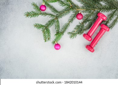 Christmas Fitness Background. Dumbbells And Spruce Branch With Christmas Decorations On A Gray Background. Copy Space. Top View.