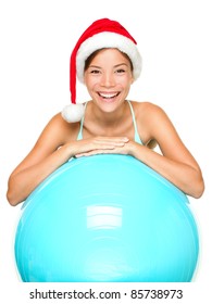 Christmas fitness woman on exercise ball wearing santa hat smiling joyful and happy. Beautiful cheerful mixed race Asian Caucasian female fitness model isolated on white background.