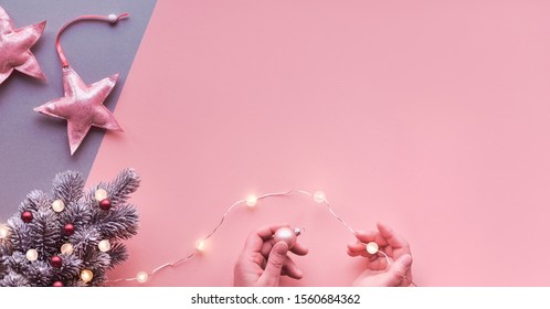 Christmas flat lay, top view on two color pink and silver paper with soft pink metallic textile stars. Hands decorating small artificial Xmas tree with light garland and magenta trinkets, copy-space. 庫存照片