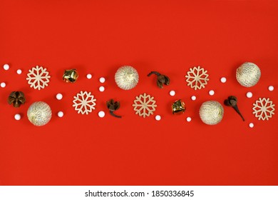 Christmas Flat Lay With Wooden Snowflake Ornaments, Golden Bells And Balls And Tree Ornament Baubles Forming Line In Middle Of Red Background 