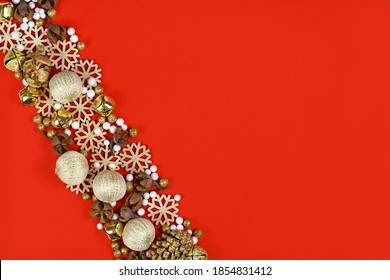 Christmas Flat Lay With Wooden Snowflake Ornaments, Golden Bells And Balls, Snowflakes And Tree Ornament Baubles Forming Line Across Red Background 