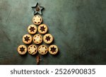 Christmas food Background with fir tree made from traditional british christmas Mince pies, anise stars and cinnamon stickes on a green table surface.  Pastry also called mincemeat or fruit pie.