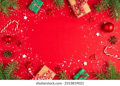 Christmas frame made of fir branches, gift boxes, festive decorations, candy and pine cones on red background. Flat lay. Happy New Year and winter holidays layout. Top view with copy space - Powered by Shutterstock