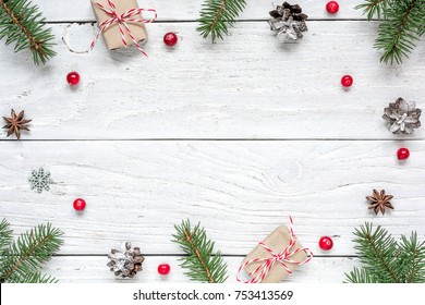 Christmas frame made of fir branches, red berries, gift boxes and pine cones on white wooden table. Christmas background. Flat lay. top view with copy space - Powered by Shutterstock