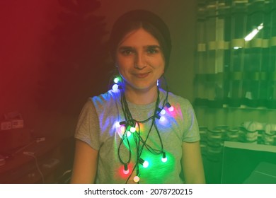 Christmas Funny Portrait. Funky Young Woman Celebrating Christmas. Young Person Having Fun On Winter Holiday Time With Colorful Lights.  Woman Wrapped In Colorful Christmas Lights. Red And Green Rave.