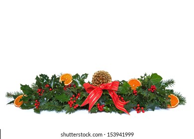 A Christmas Garland Made From Fresh Holly With Red Berries, Dried Orange Segments, Green Ivy, Conifer Sprigs And Pine Cone, Finished Off With A Red Ribbon And Bow. Isolated On A White Background.