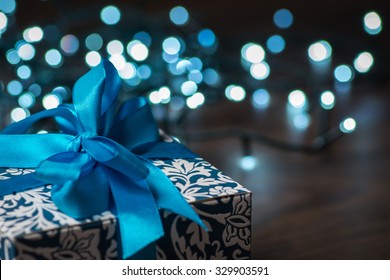 Christmas Gift Box With Blue Bow And Bokeh Lights On Wooden Surface