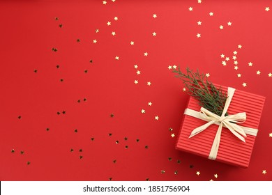 Christmas gift box with coniferous twigs and shiny confetti on red background, flat lay. Space for text