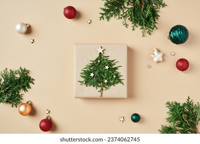 Christmas gift box decorated fir branches and xmas balls ornaments on beige background. Flat lay, top view.