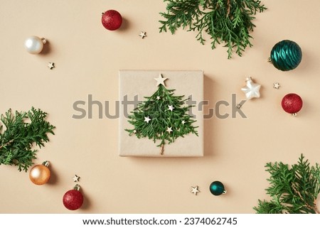 Christmas gift box decorated fir branches and xmas balls ornaments on beige background. Flat lay, top view.