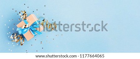 Christmas gift box with golden decorations and sparkles on blue bacground. Gift box tied with blue ribbon. Holiday banner.