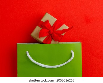 Christmas Gift Box In Green Paper Shopping Bag On Red Background - Overhead View Flat Lay, Top View, Minimalism