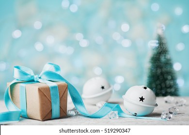 Christmas Gift Box, Jingle Bell And Blurred Fir Tree Against Blue Bokeh Background. Holiday Greeting Card.