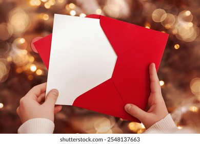 Christmas Gift Certificate with Red Envelope in Hands on Christmas Lights Background. Christmas Sale, Wish List, Greeting Card concept. - Powered by Shutterstock