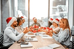 Christmas Gift Exchange At Work. A Group Of Happy Business People Are Sitting At A Table And Exchanging Gifts. Secret Santa.