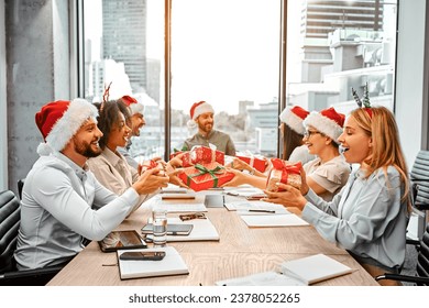 Christmas gift exchange at work. A group of happy business people are sitting at a table and exchanging gifts. Secret Santa. - Powered by Shutterstock