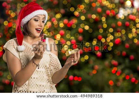 Christmas Gift - woman opening gift surprised and happy, Young beautiful smiling woman in Santa hat. Funny cute photo of Brazilian / Brazilian woman over christmas background

