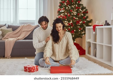 Christmas gift wrapping. An attractive mixed race Asian Caucasian woman and handsome man wrap present during Christmas and New Year preparations in front of the Christmas tree. - Powered by Shutterstock