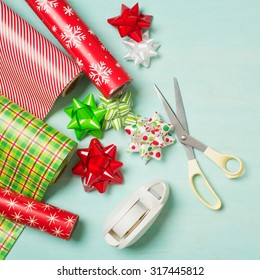 Christmas Gift Wrapping Party Time With Colorful Paper, Ribbon Bows, Scissors And Tape On Cyan Blue Shabby Chic Wood Board Background With Square Crop And Room Or Space For Copy, Text, Your Words.  