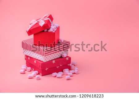 Christmas gifting theme image with a stack of gifts wrapped in different red designs, full of pink tiny marshmallows, on a pink paper background.