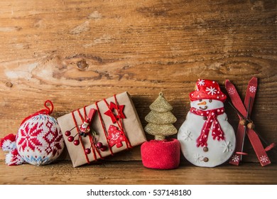 Christmas Gifts. Santa Claus Puts Gifts. Snowman With Ski, Golden Christmas Tree, Gift Box And Knitted Round Toy On Wooden Background