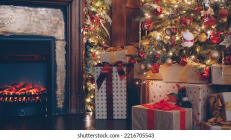 Christmas Gifts Under Decorated Tree In Dark Room Illuminated With Fire From Fireplace, House Is Ready For Traditional Winter Celebration. No People Are Visible.