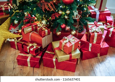 Christmas Gifts Wrapped In Classic Red Paper, Background With Xmas Lights Bokeh Of Blurred Under Christmas Tree. Copy Space