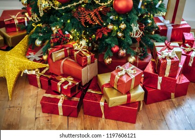 Christmas Gifts Wrapped In Classic Red Paper, Background With Xmas Lights Bokeh Of Blurred Under Christmas Tree. Copy Space