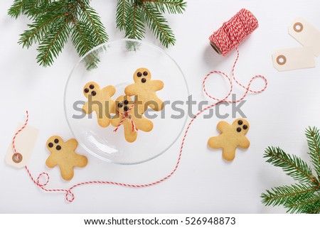 Christmas gingerbread butter cookies on glass plate, fir branches and striped decorative rope on the white wooden table. Top view.