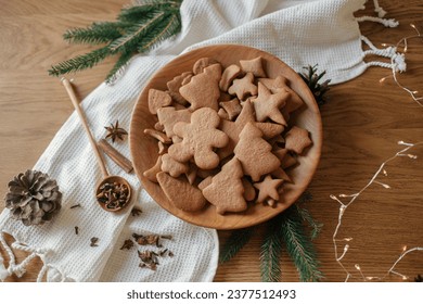 Christmas gingerbread cookies in wooden plate on rustic table flat lay with fir branches, pinecone, spices. Merry Christmas! Delicious fresh gingerbread cookies close up, atmospheric holiday