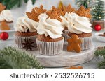 Christmas gingerbread cupcakes with cream cheese frosting and mini gingerbread cookies on top on a wooden board. Festive dessert