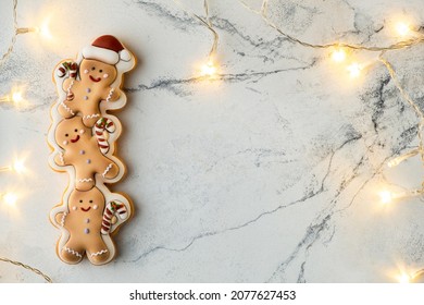 Christmas gingerbread man cookies on the white marble background decorated with warm garland. Merry Christmas and Happy New Year.