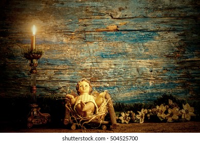 Christmas greeting card, baby Jesus in his crib and vintage candle, rustic wooden background with copy space for text