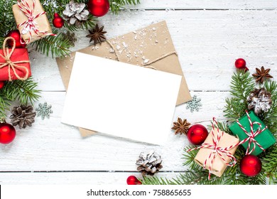 Christmas Greeting Card With Fir Tree Branches, Decorations And Gift Boxes Over White Wooden Background. Mock Up. Flat Lay