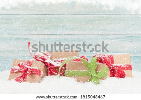 Christmas greeting card with gift boxes in snow in front of wooden wall and copy space for your xmas greetings