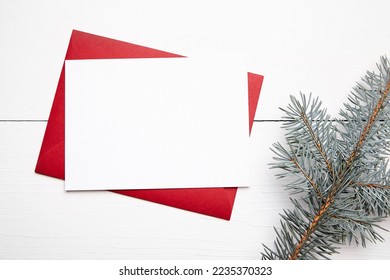 Christmas greeting card mockup with red envelope and fresh green fir tree branch on white wooden background, top view, flat lay. Winter holiday card mock up - Powered by Shutterstock