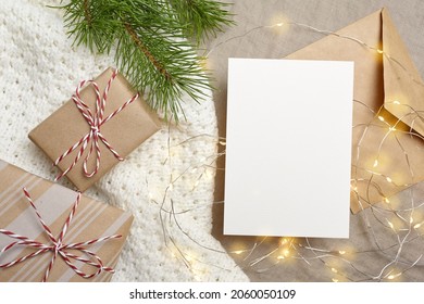 Christmas Greeting Card Mockup. White Blank Card With Gift Boxes And Glowing Light Garland