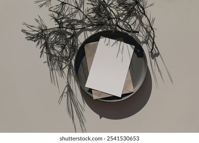 Christmas greeting card mockup. Winter stationery. Blank paper invitation on ceramic plate with pine tree branches in sunlight. Long shadows, beige table background. festive holiday flatlay, top view - Powered by Shutterstock