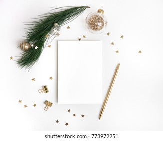 Christmas Greeting Card Template In Gold. Empty Paper Mock Up, Fir Tree Branch With Glass Ball Decorations, Star Confetti, Pen On White Background. New Year Flat Lay, Top View, Copy Space