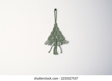 Christmas handmade macrame tree ornament winter holiday, green eco macramé Christmas tree decorations in boho style hanging. tree made from cotton green string on white wall background  - Shutterstock ID 2233327537