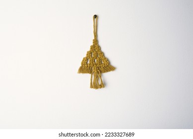 Christmas handmade macrame tree ornament winter holiday, gold eco macramé Christmas tree decorations in boho style. tree made from cotton gold string on white wall background  - Shutterstock ID 2233327689