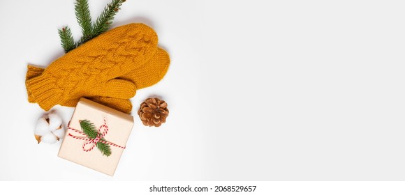 Christmas holiday composition of mustard knitted mittens with xmas gift box and pine cone decor on white background. Winter, new year concept. Flat lay, top view