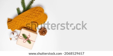 Christmas holiday composition of mustard knitted mittens with xmas gift box and pine cone decor on white background. Winter, new year concept. Flat lay, top view
