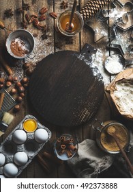 Christmas Holiday Cooking And Baking Ingredients. Cookie Molds, Spices, Flour, Eggs, Cocoa Powder, Sugar, Honey, Nuts On Rustic Wooden Background With Dark Wood Board In Center. Top View, Copy Space