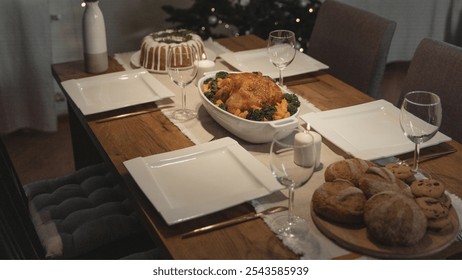 Christmas holiday dinner, light wood table, white plates, wine glasses, roasted chicken, vegetables, candle decor, bread rolls, chocolate chip cookies, cozy gray chairs, inviting - Powered by Shutterstock