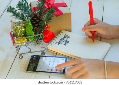 Christmas holiday shopping lists and sale season concept. Hand holding pen using calculator. to write shopping lists for friends and family planning budget for holiday with shopping cart and gift box