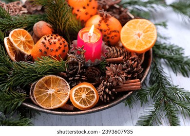Christmas holiday. Winter ritual for Yule sabbat. Candle, deer amulet, cinnamon, nuts, cones, decorated oranges and dry orange slices, fir branches in plate on table. Festive winter season.
