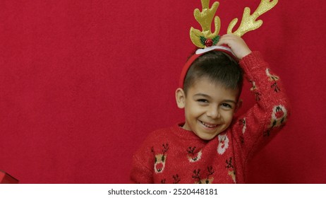 Christmas holidays. Cute boy child adjusting deer antlers isolated on red background. High quality photo - Powered by Shutterstock